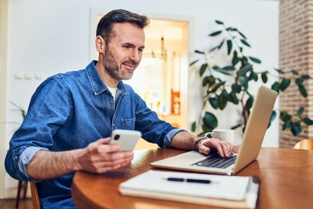 Caucasian man holding mobile phone sitting in living room logging in to Monroe Savings Bank account